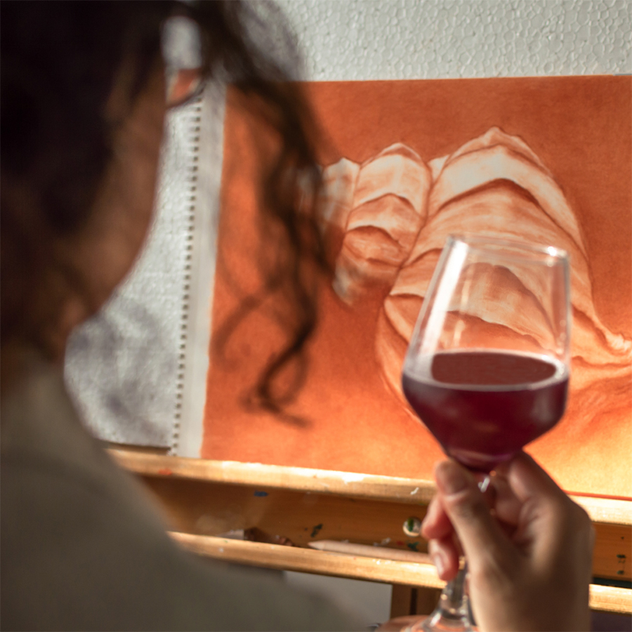 Woman holding a glass of wine while she paints on a canvas